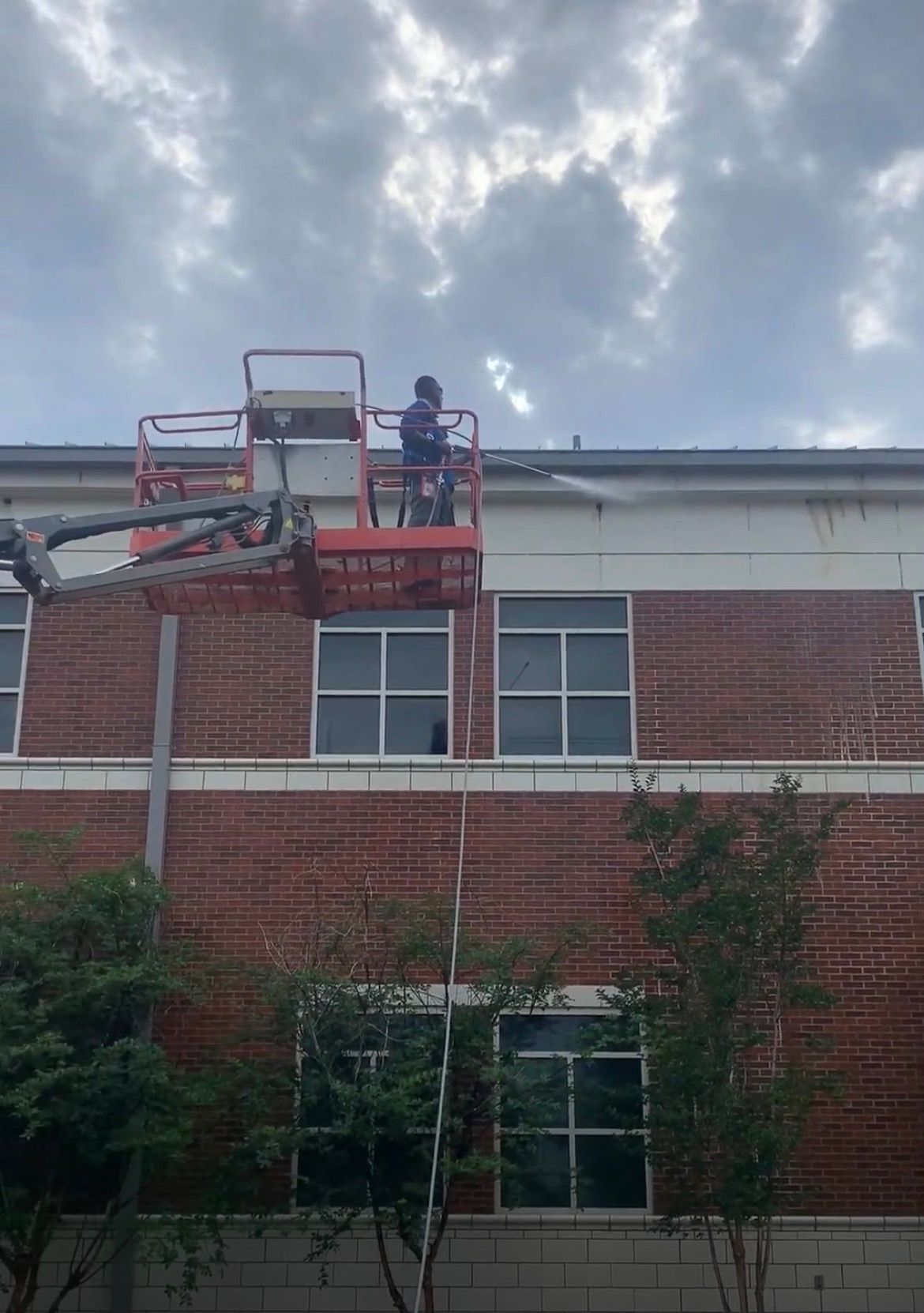 Rain falling on a terracotta tile roof with a brown gutter and green foliage in the background.