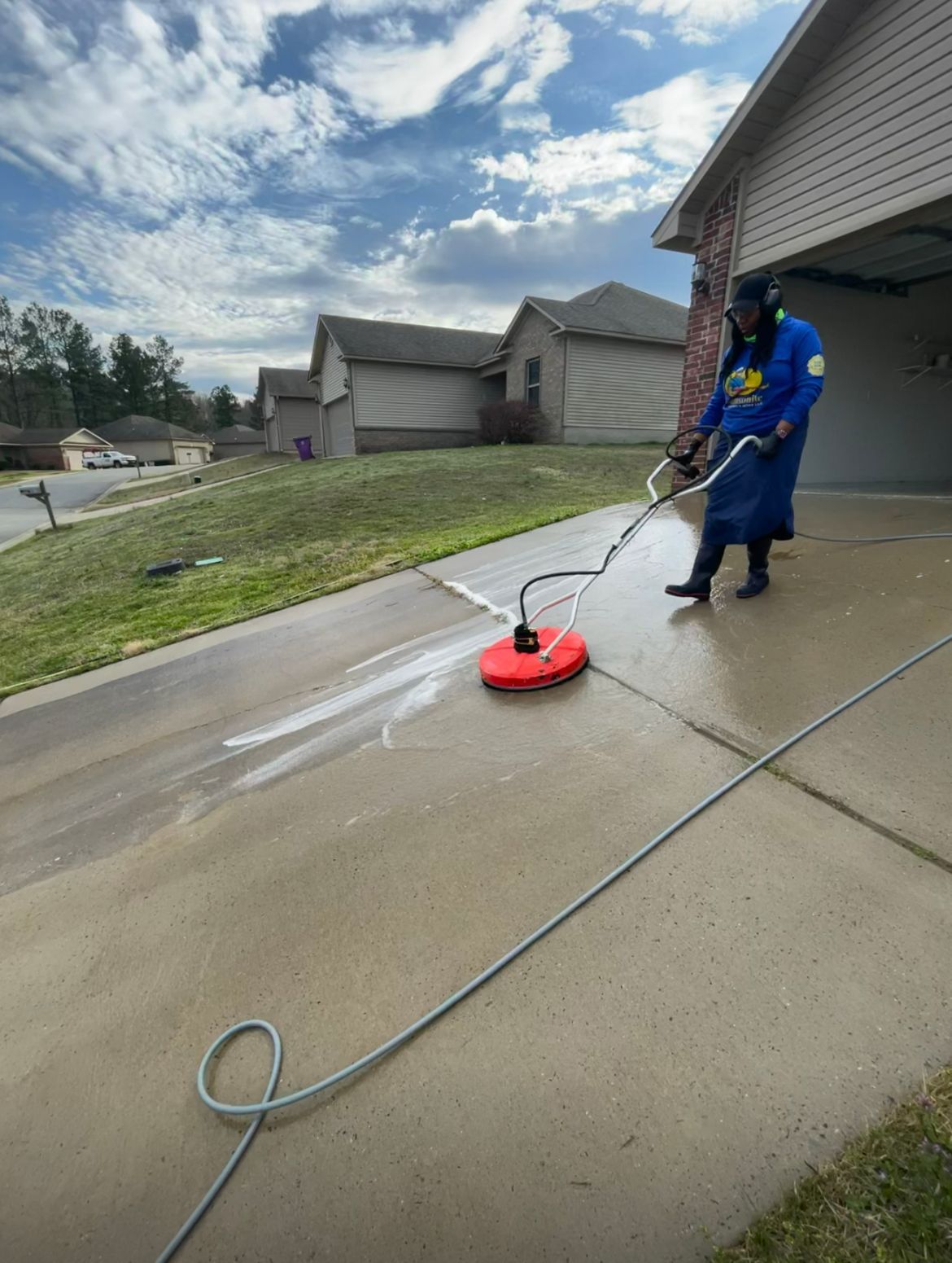 Person pressure washing a driveway with a red surface cleaner. Cloudy sky.