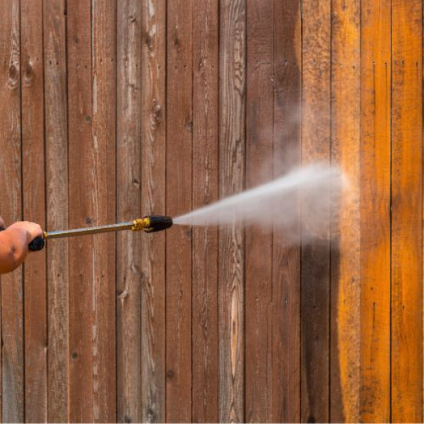 Log cabin with a white picket fence and sunflowers, under a cloudy sky.