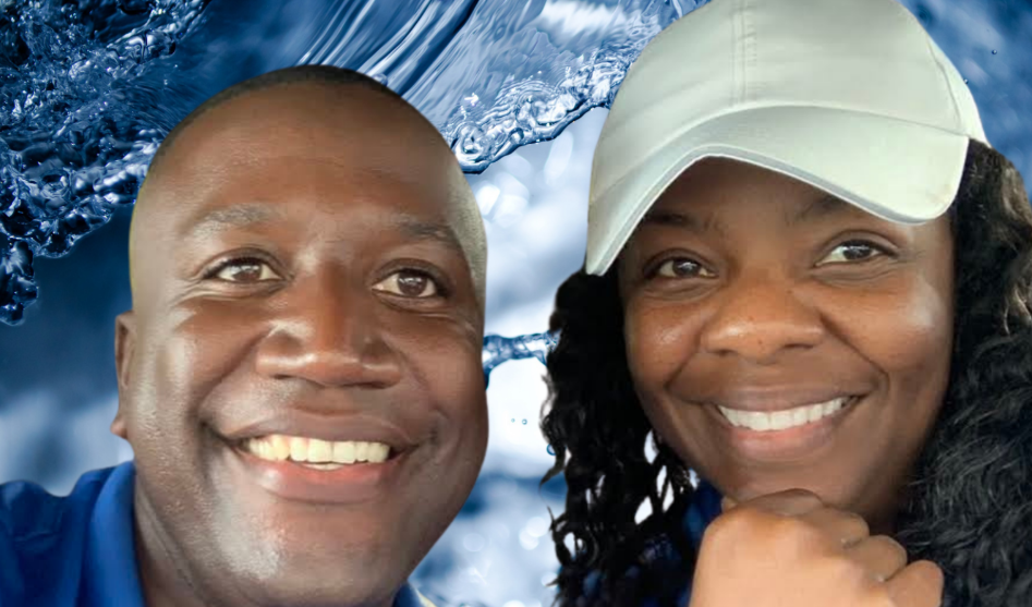 Smiling Black couple; man in blue, woman in a white cap, in front of a blue water background.