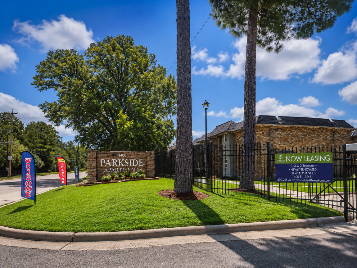 Entrance sign for Parkside apartments with green lawn, black fence, and trees under a blue sky