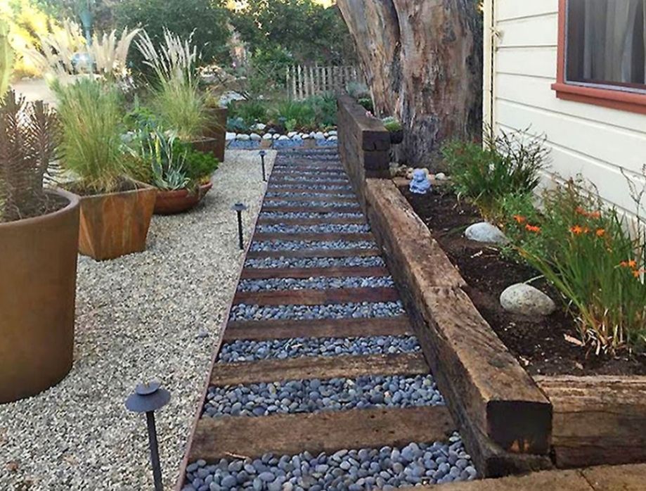 Wooden pathway with pebbles and plants alongside a house, lit by solar lights.