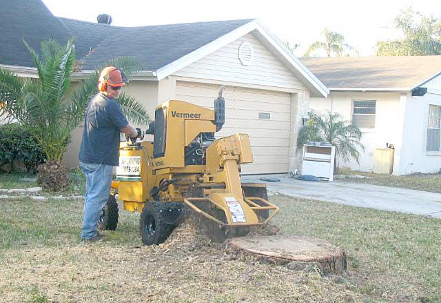 a man is using a machine to remove a tree stump in front of a house .