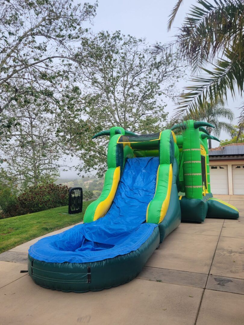 Green-and-yellow inflatable water slide with a blue splash pool in a grassy backyard