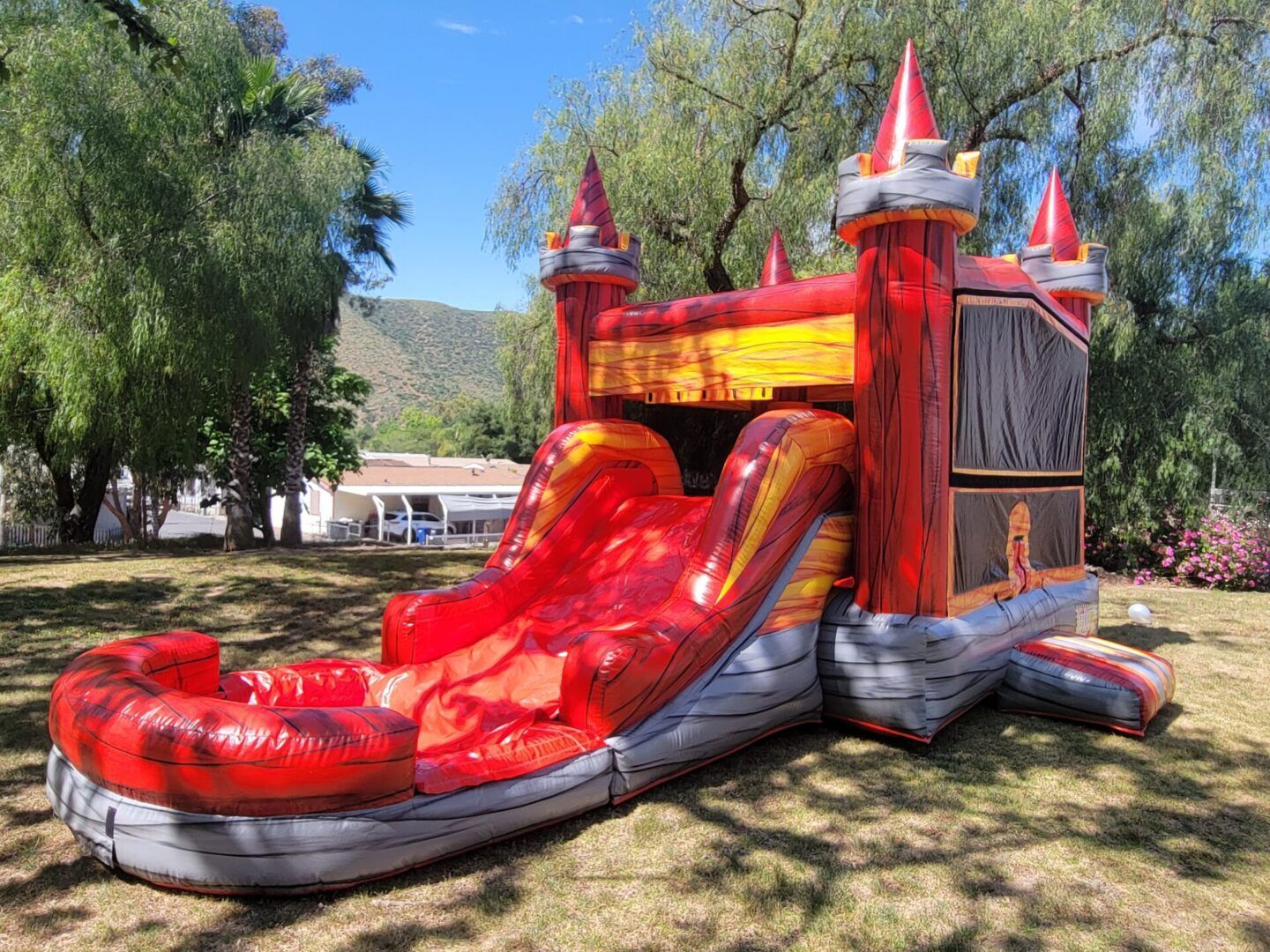 Red and yellow inflatable castle slide at a sunny outdoor event on grass