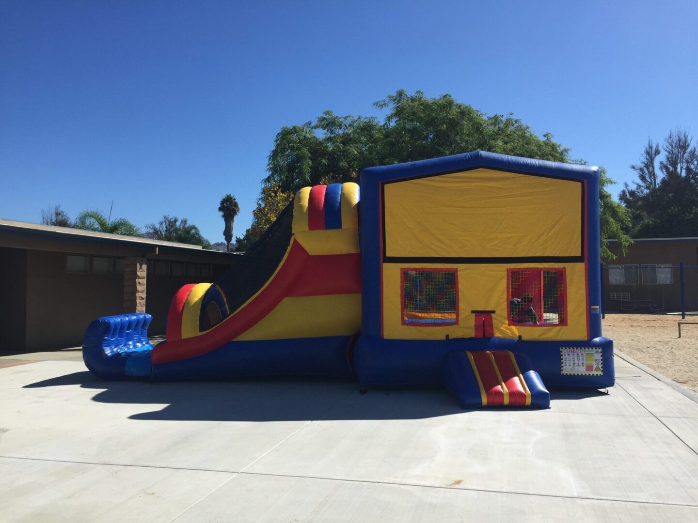 Colorful inflatable bounce house with slide and entrance on a sunny paved lot