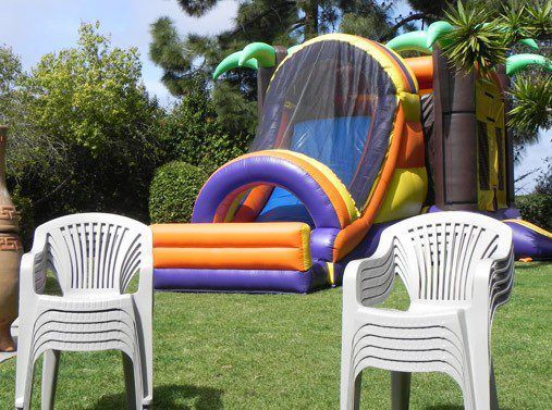 Inflatable bouncy castle in a grassy yard, with two white plastic chairs in the foreground.