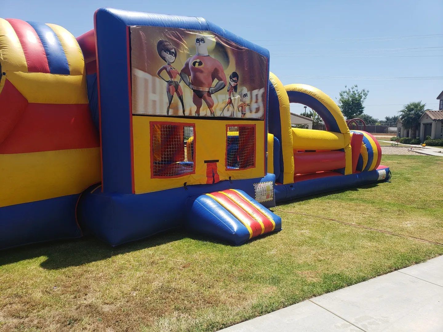 Colorful inflatable bouncy castle with a cartoon panel set up on a grassy field outdoors