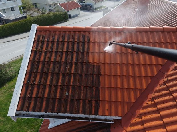 Power washing a red tile roof, removing dark grime to reveal clean tiles.