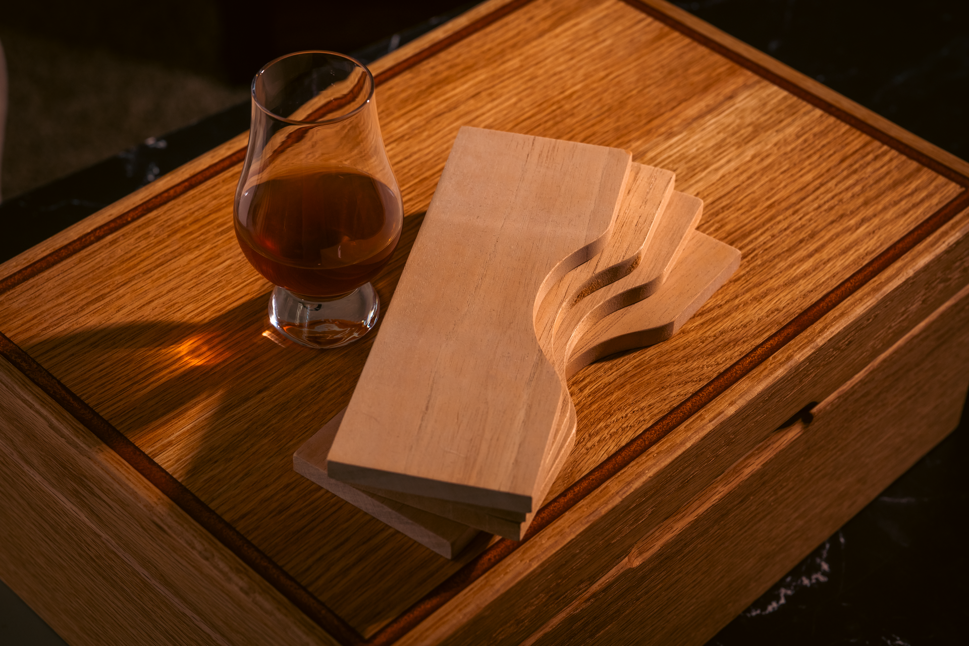 Glass of amber liquid next to wooden planks with a cut-out design on a wooden box.