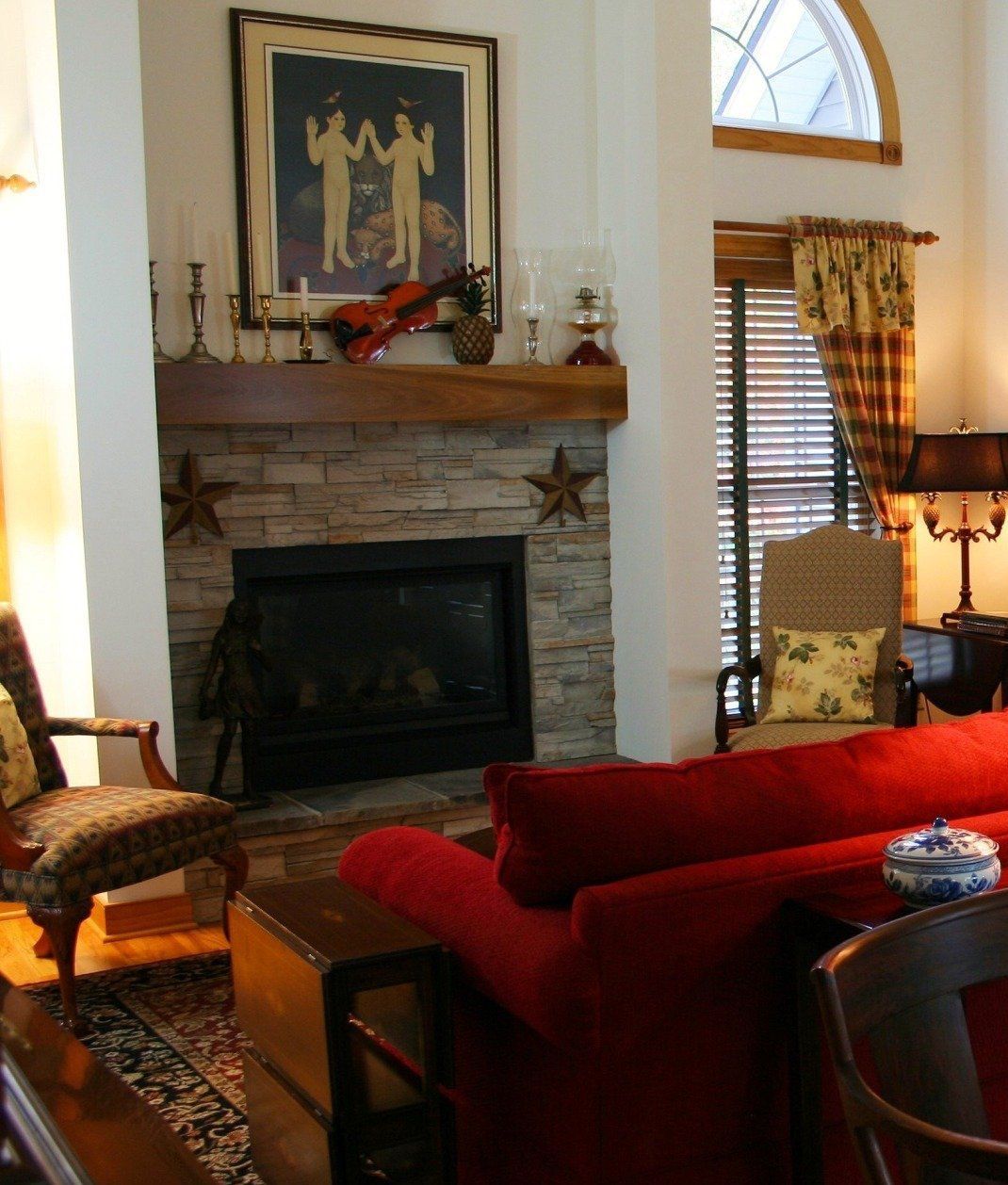 Living room with stone fireplace, red couch, wooden accents, and art.
