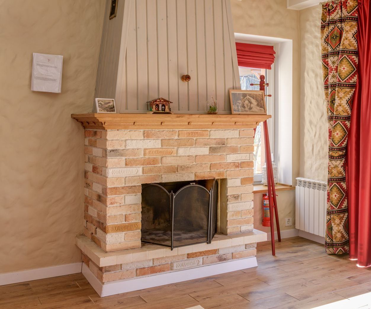 Brick fireplace with wooden mantel, metal screen, and decorative curtains.