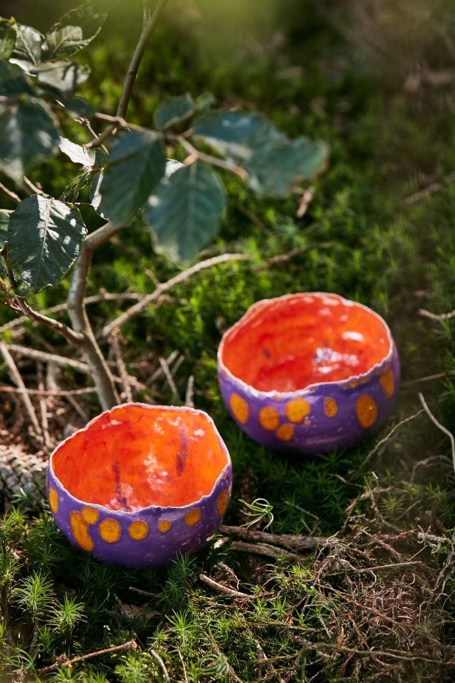 Zwei violette und orangefarbene Schalen stehen auf einer moosigen Oberfläche.