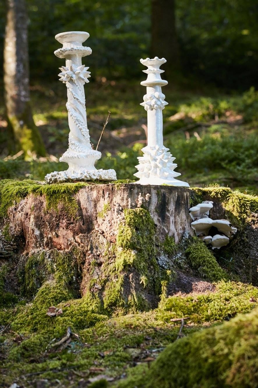 Zwei weiße Kerzenhalter stehen auf einem moosbedeckten Baumstumpf.