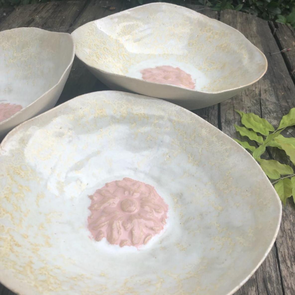 Drei weiße Schüsseln mit einer rosa Blume darauf stehen auf einem Holztisch.