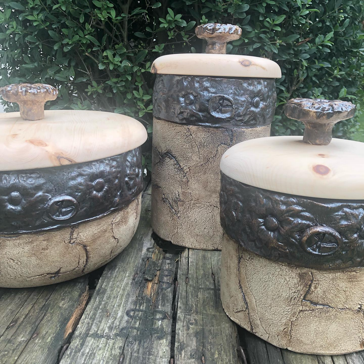 Drei Keramikgefäße mit Holzdeckeln stehen auf einem Holztisch.