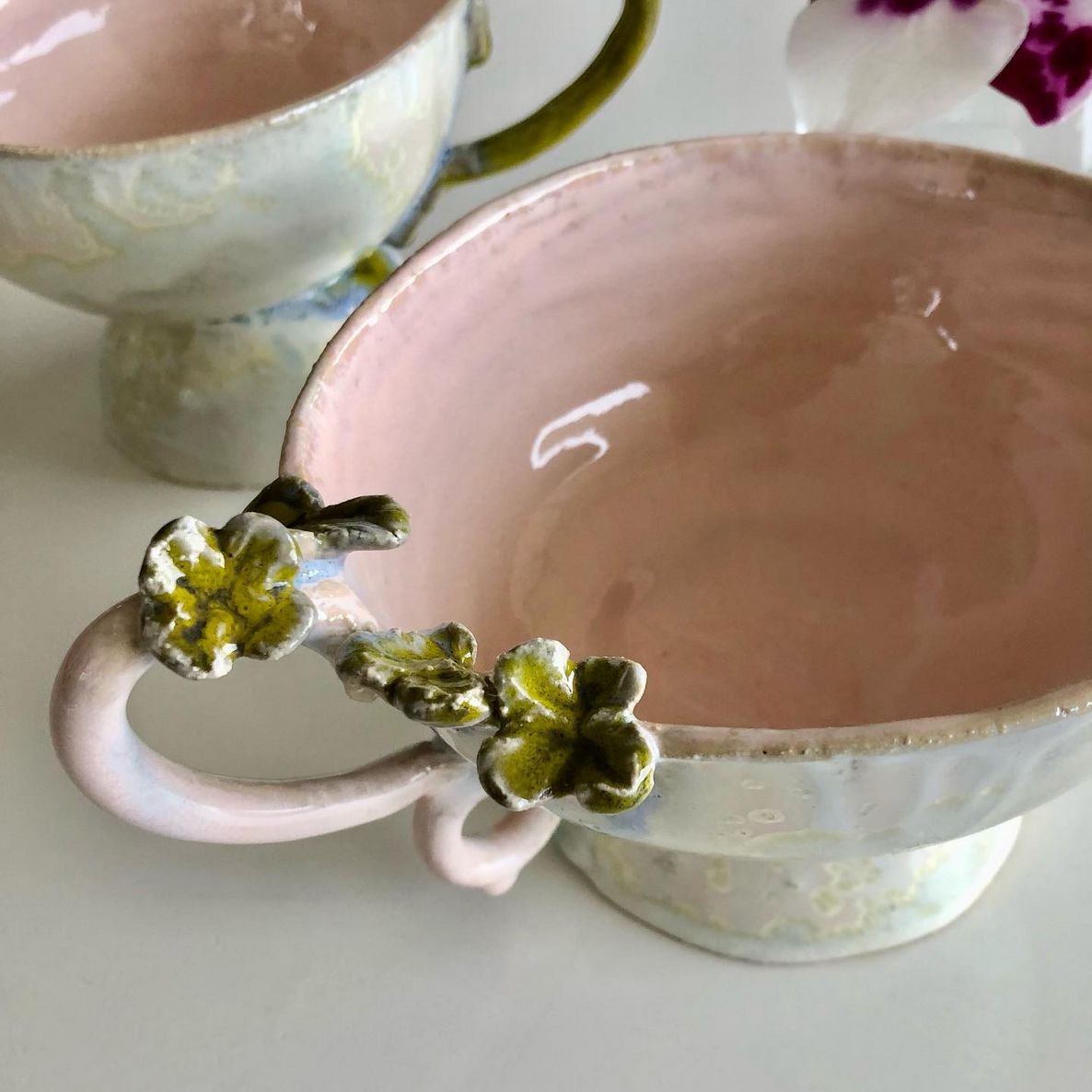 Zwei Tassen mit Blumen an den Henkeln stehen auf einem Tisch