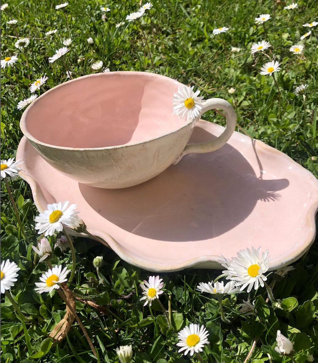 Eine Tasse und Untertasse liegen auf einem rosa Teller im Gras