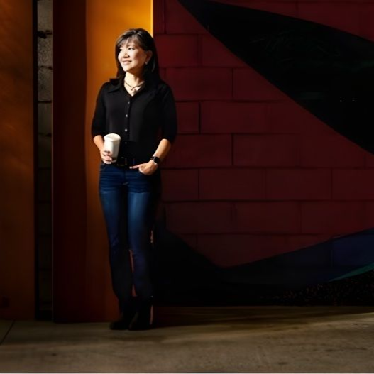 Woman standing, holding a cup, against a brick wall with abstract art.