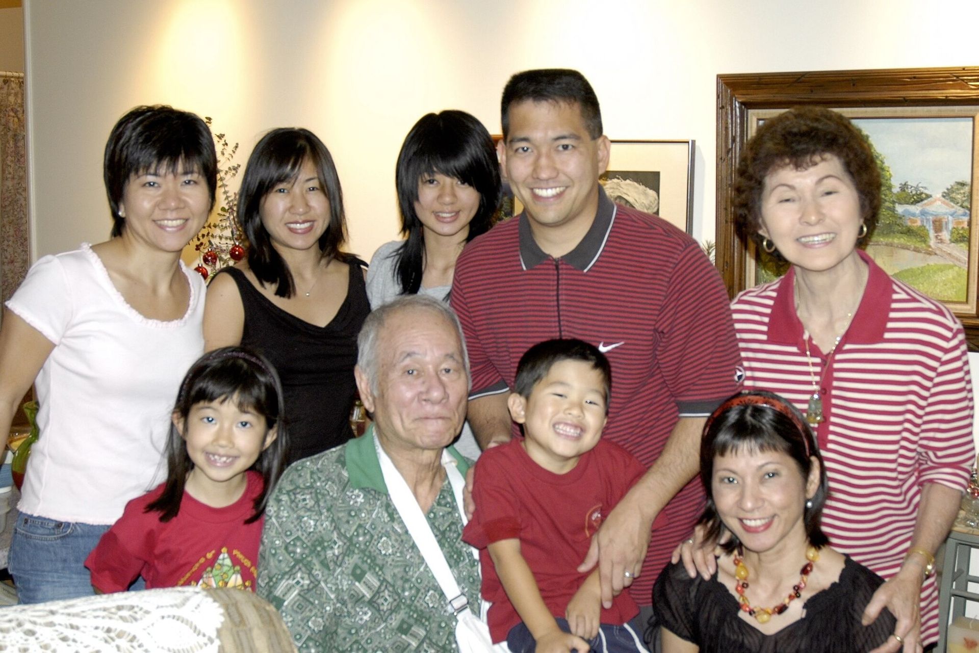 Family portrait, smiling, gathered together indoors. Includes children, adults, and an elderly person.