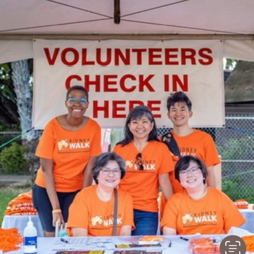 Volunteers at a Kidney Walk check-in table wearing orange shirts. Banner says 