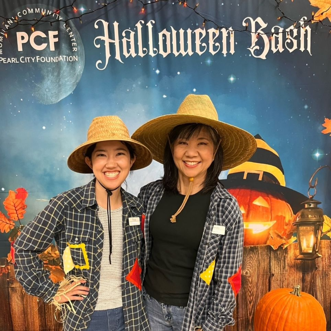 Group of people in red shirts and vests smile at an outdoor table. Holding drinks and a yellow chicken toy.