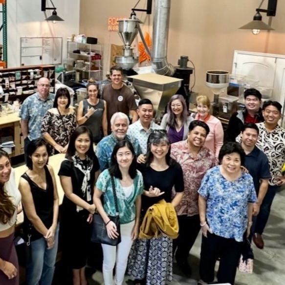 Group of people smiling in a coffee roasting facility, with equipment in the background.