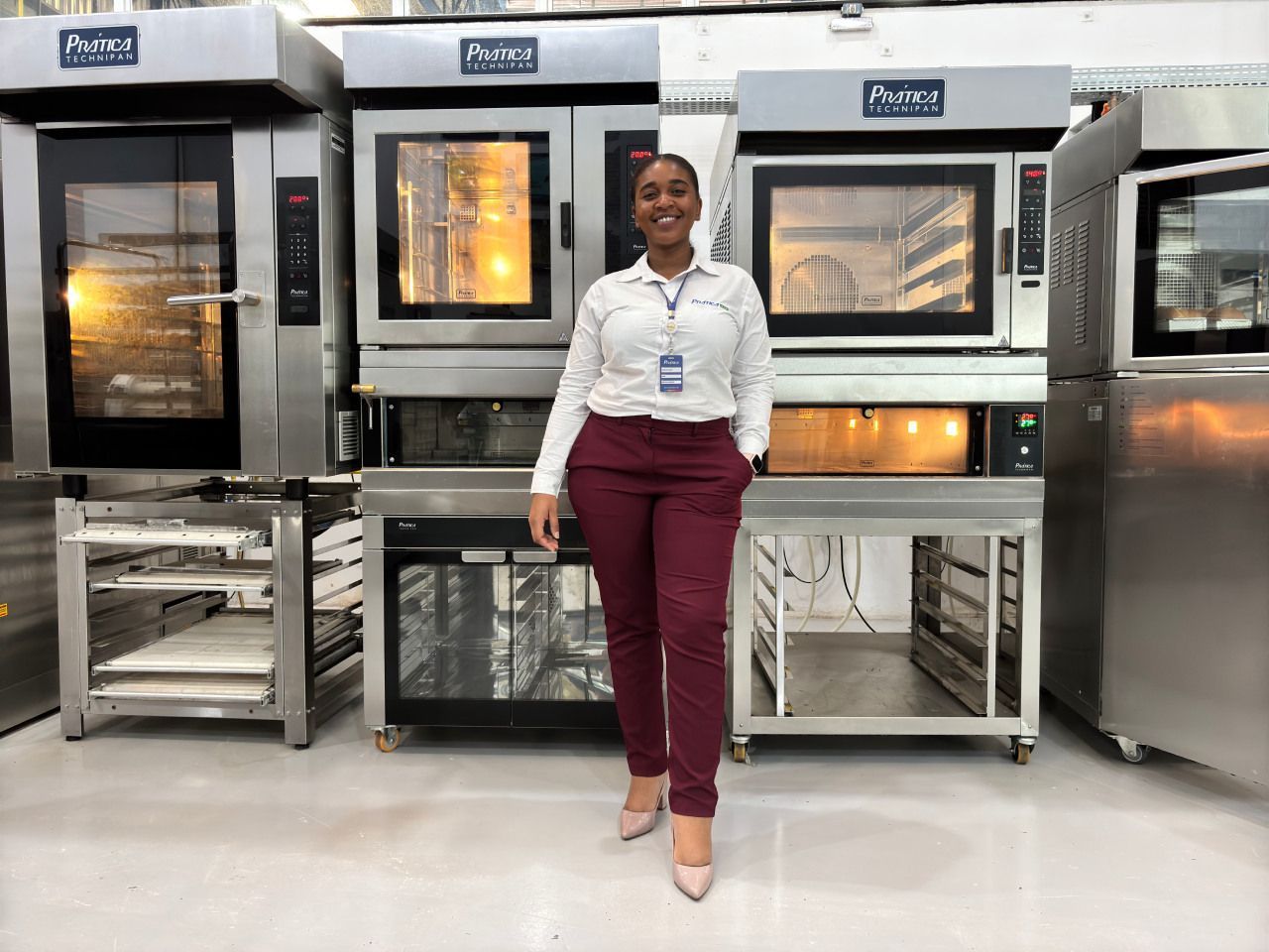 Uma mulher está parada em frente a uma fileira de fornos em uma cozinha.