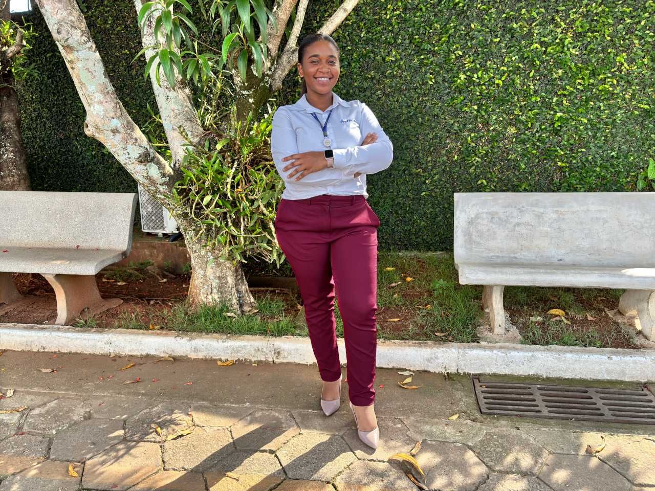 Uma mulher está parada em frente a um banco com os braços cruzados.