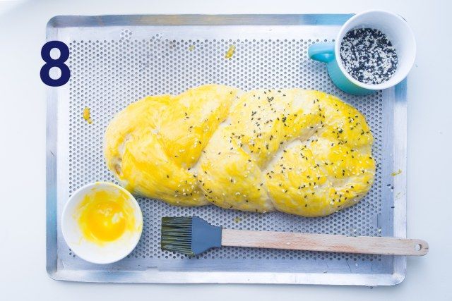 Um pedaço de pão está em uma bandeja ao lado de uma tigela de manteiga e um pincel.