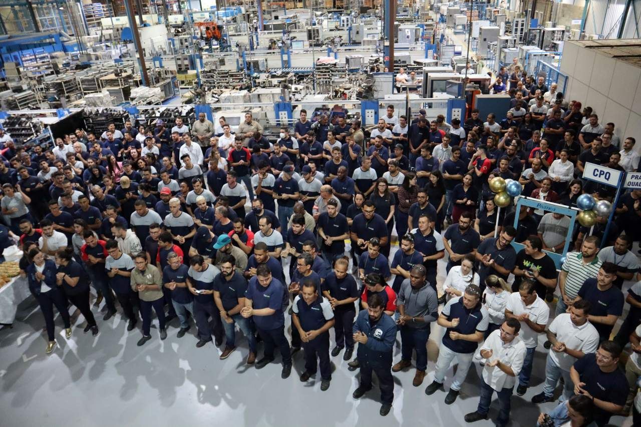 Um grande grupo de pessoas está em uma fábrica.