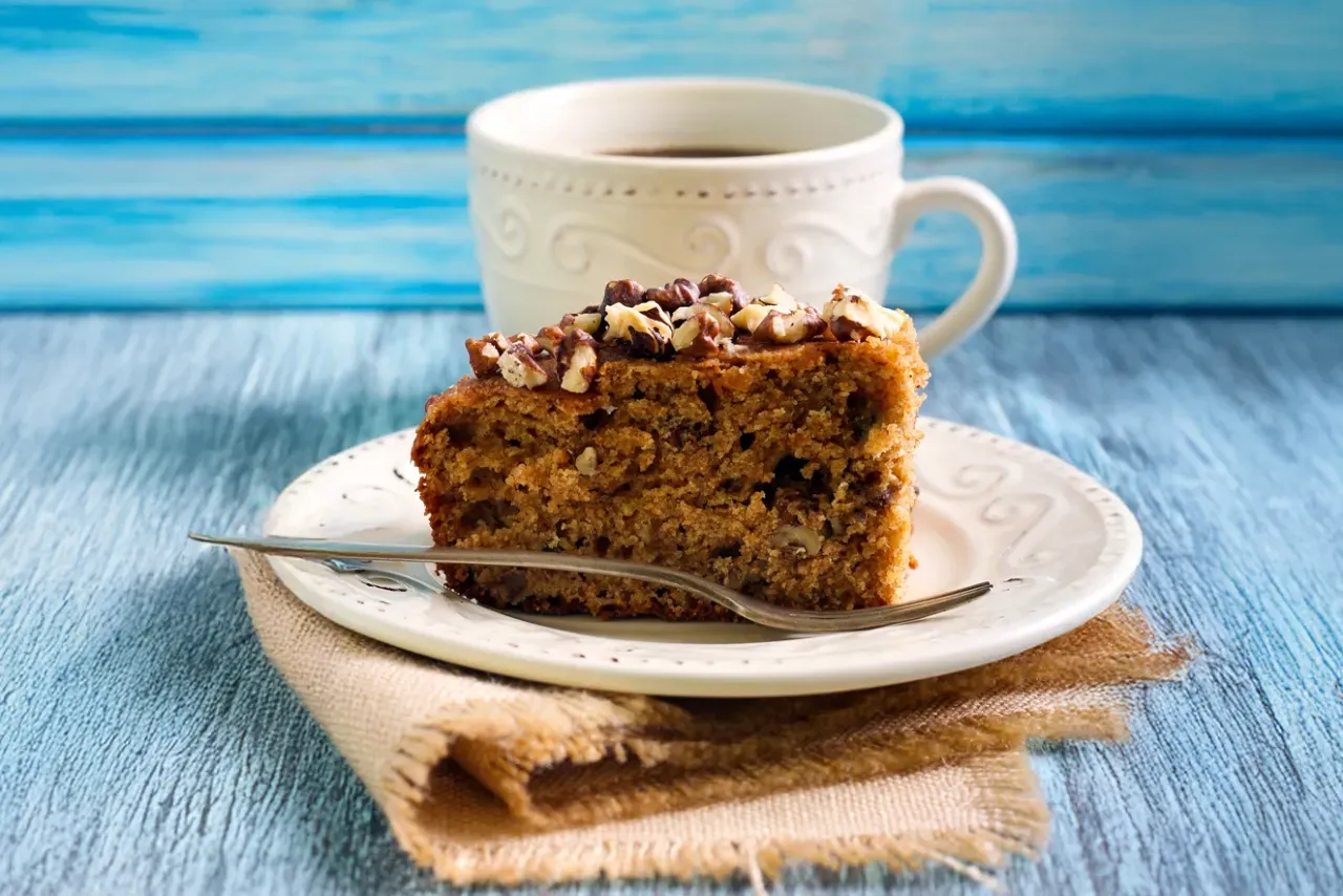 Uma fatia de bolo de cenoura está em um prato ao lado de uma xícara de café.