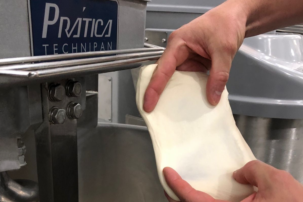 Uma pessoa está segurando um pedaço de massa na frente de uma batedeira prática