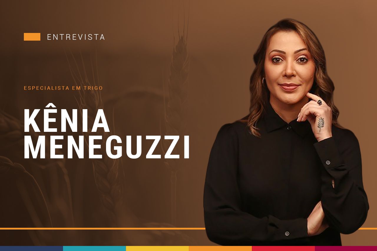 Uma mulher de camisa preta está parada em frente a um fundo marrom com o nome Kenia Meneguzzi escrito nele