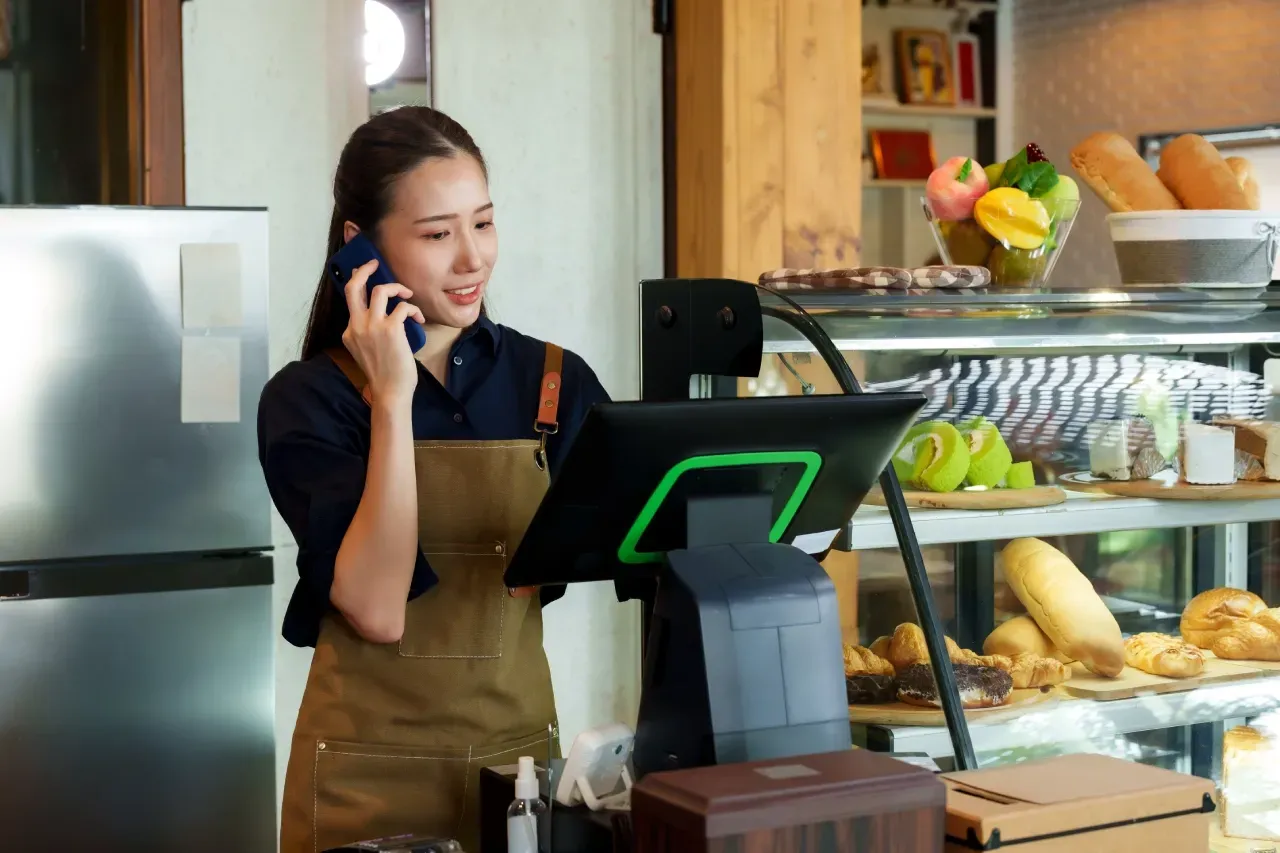 Uma mulher está falando ao celular enquanto está no balcão de um restaurante.