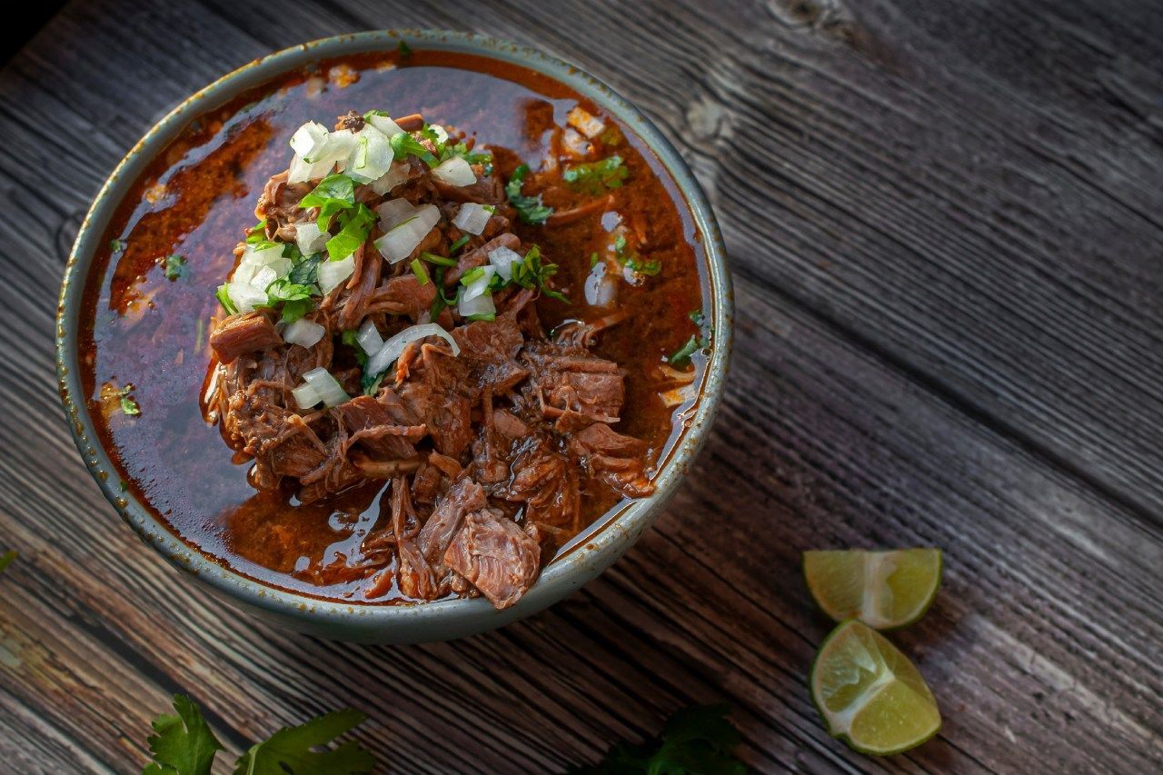 Uma tigela de sopa com carne e vegetais em uma mesa de madeira.