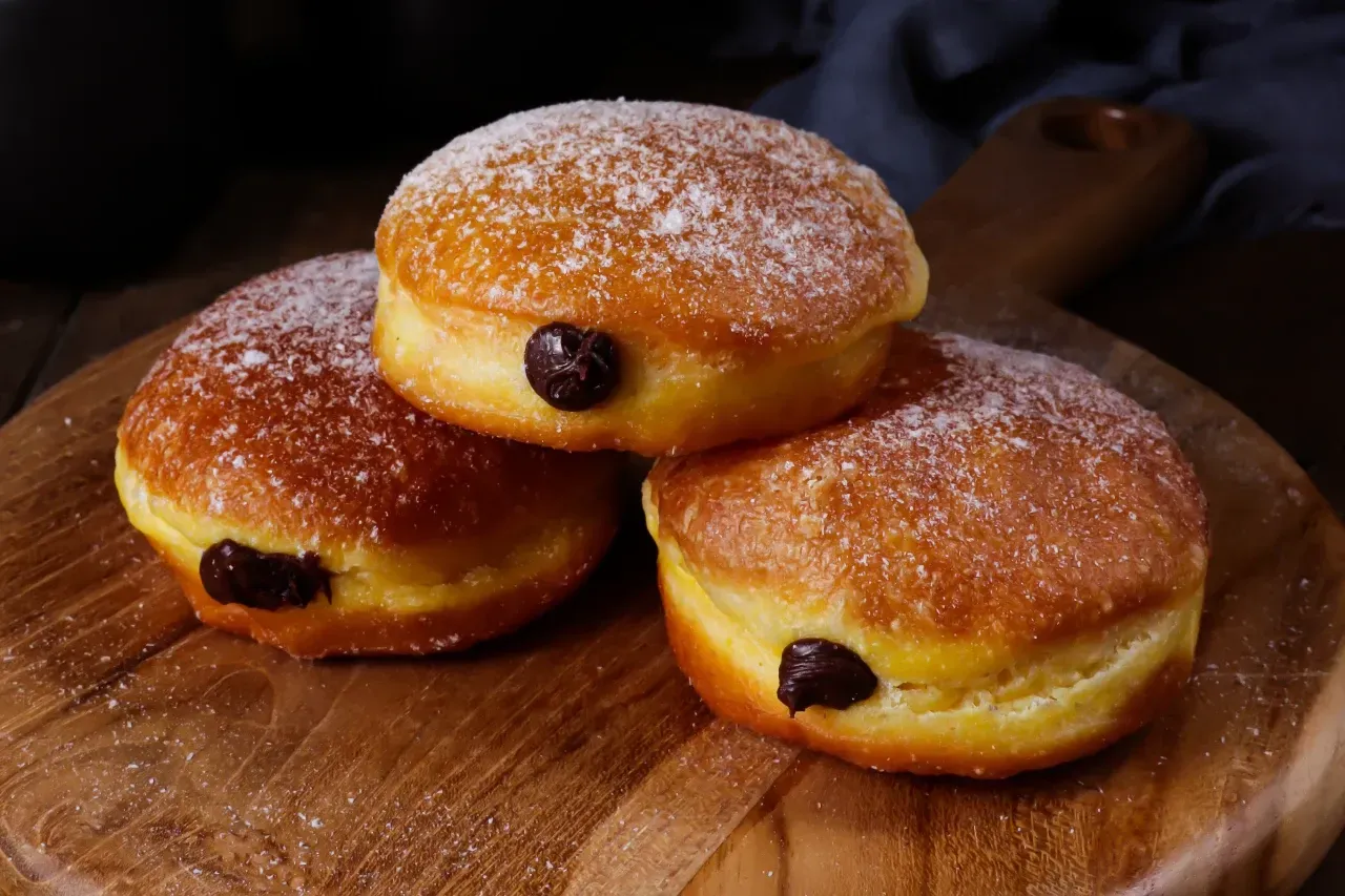 Três donuts são empilhados uns sobre os outros em uma tábua de corte de madeira.