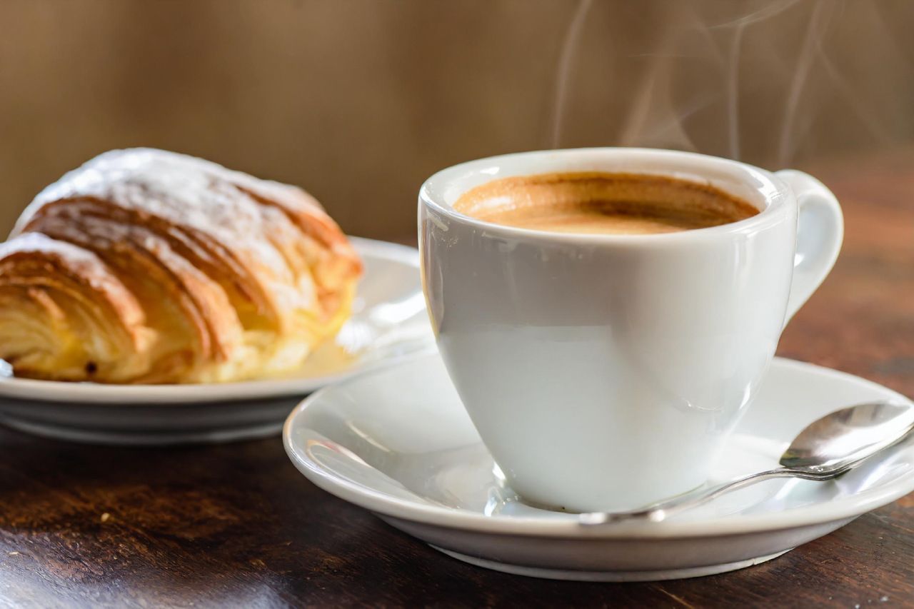 Uma xícara de café e um croissant em uma mesa de madeira.