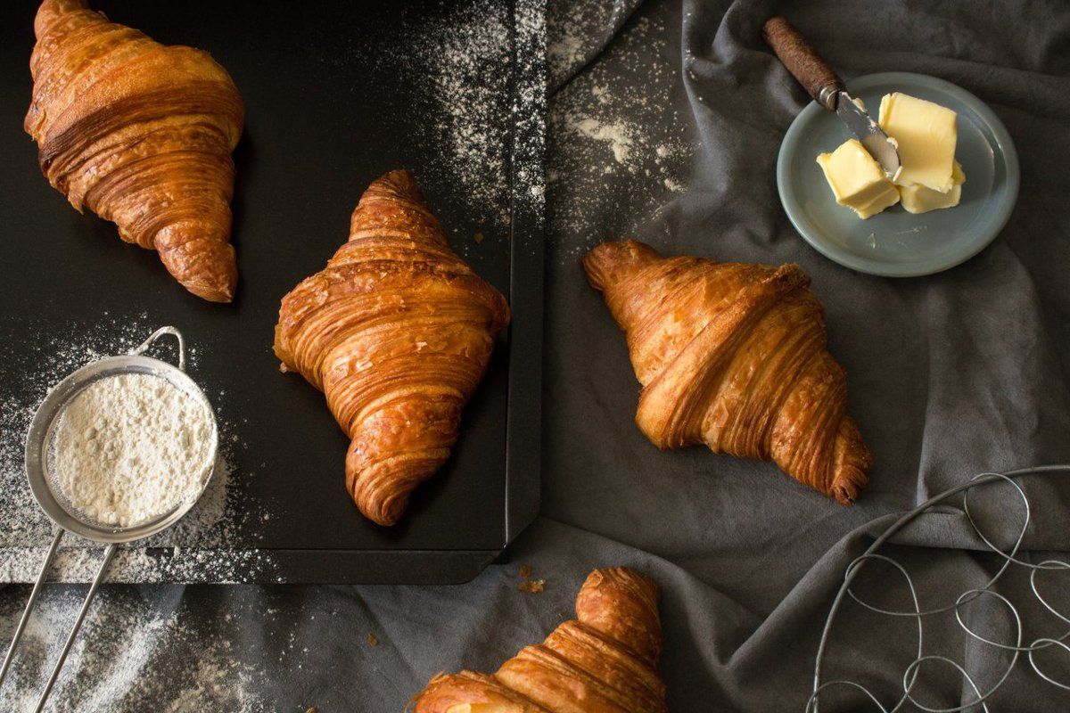 Três croissants estão sobre uma mesa ao lado de uma tigela de farinha.
