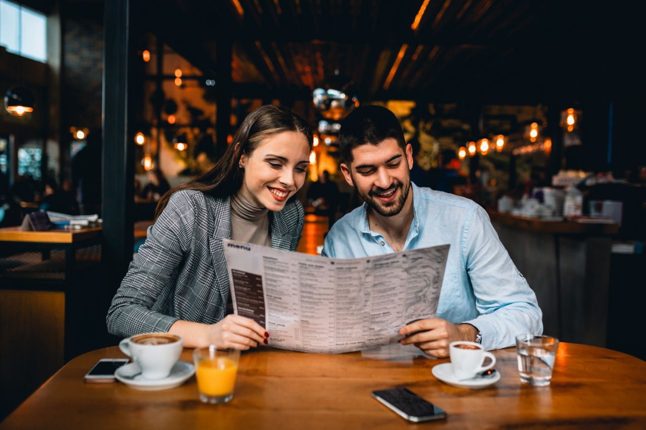 Um homem e uma mulher estão sentados à mesa de um restaurante olhando o cardápio.