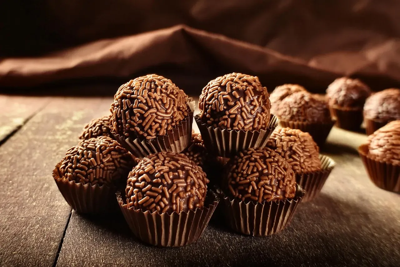 brigadeiro tradicional com confeitos de chocolate sobre mesa de madeira e fundo marrom