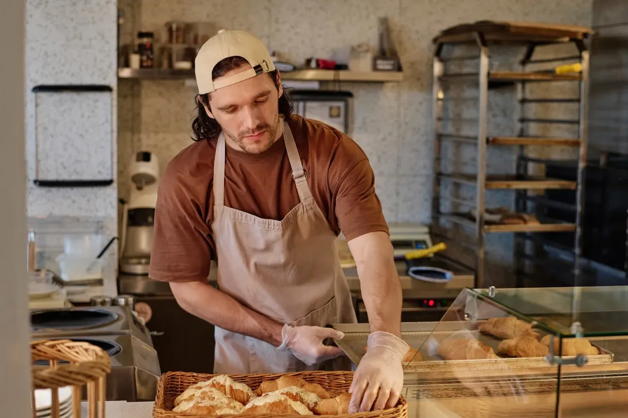 jovem padeiro organizando produtos em uma vitrine de padaria artesanal