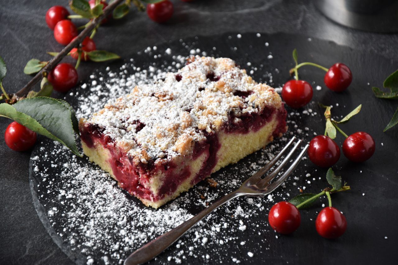 Um pedaço de bolo com cerejas e açúcar de confeiteiro em um prato com um garfo.