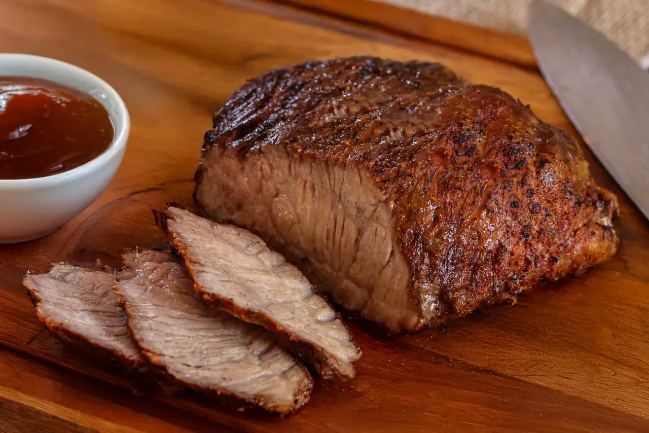 Cupim assado fatiado sobre tábua de madeira com faca e tigela de ketchup ao lado.