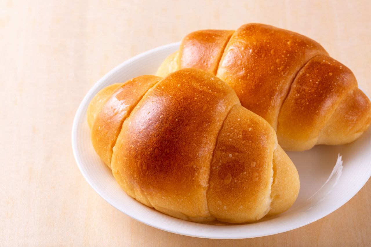 Dois dinner rolls em um prato branco sobre uma mesa.