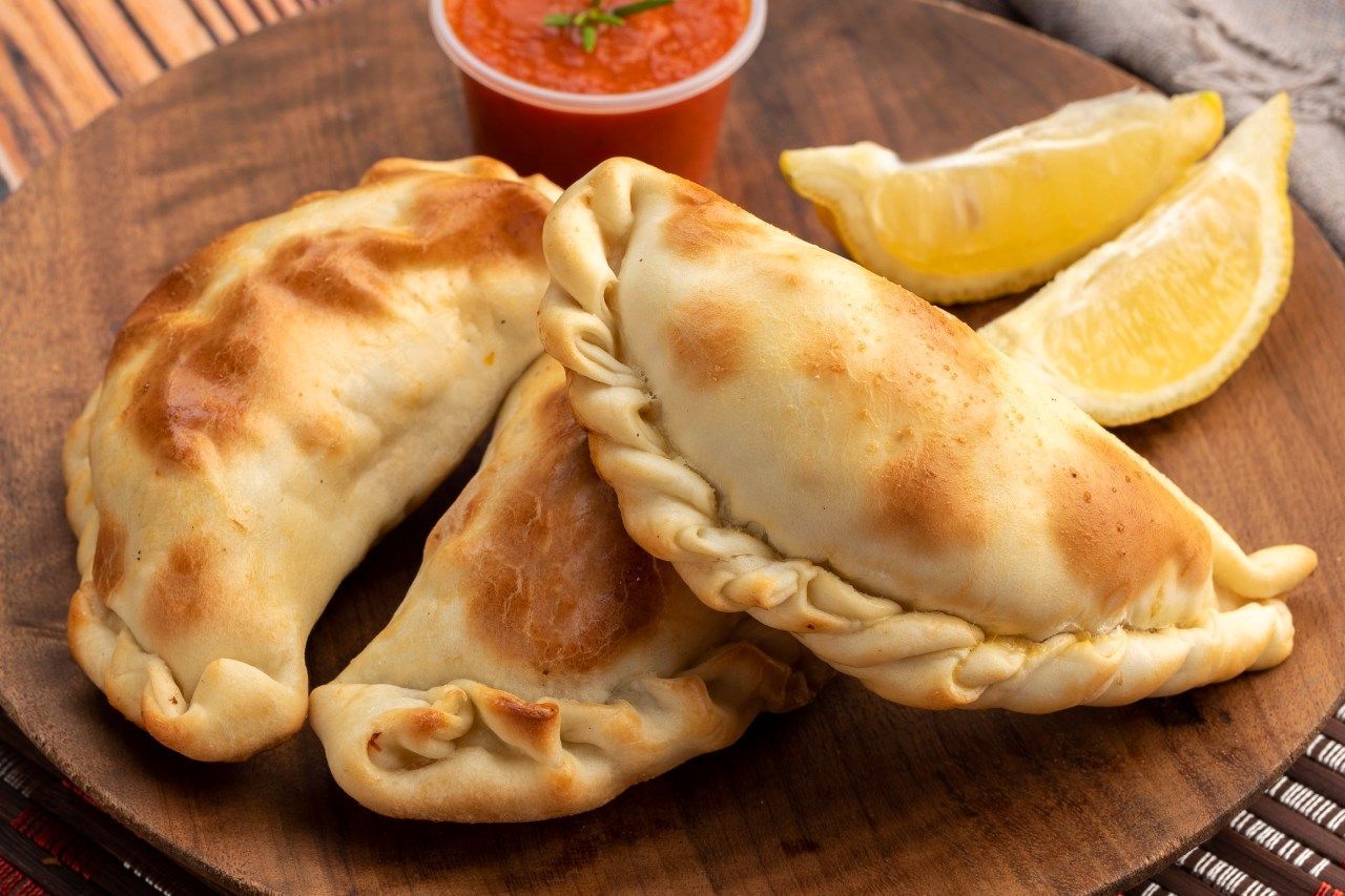 Uma tábua de corte de madeira coberta com empanadas, rodelas de limão e salsa.