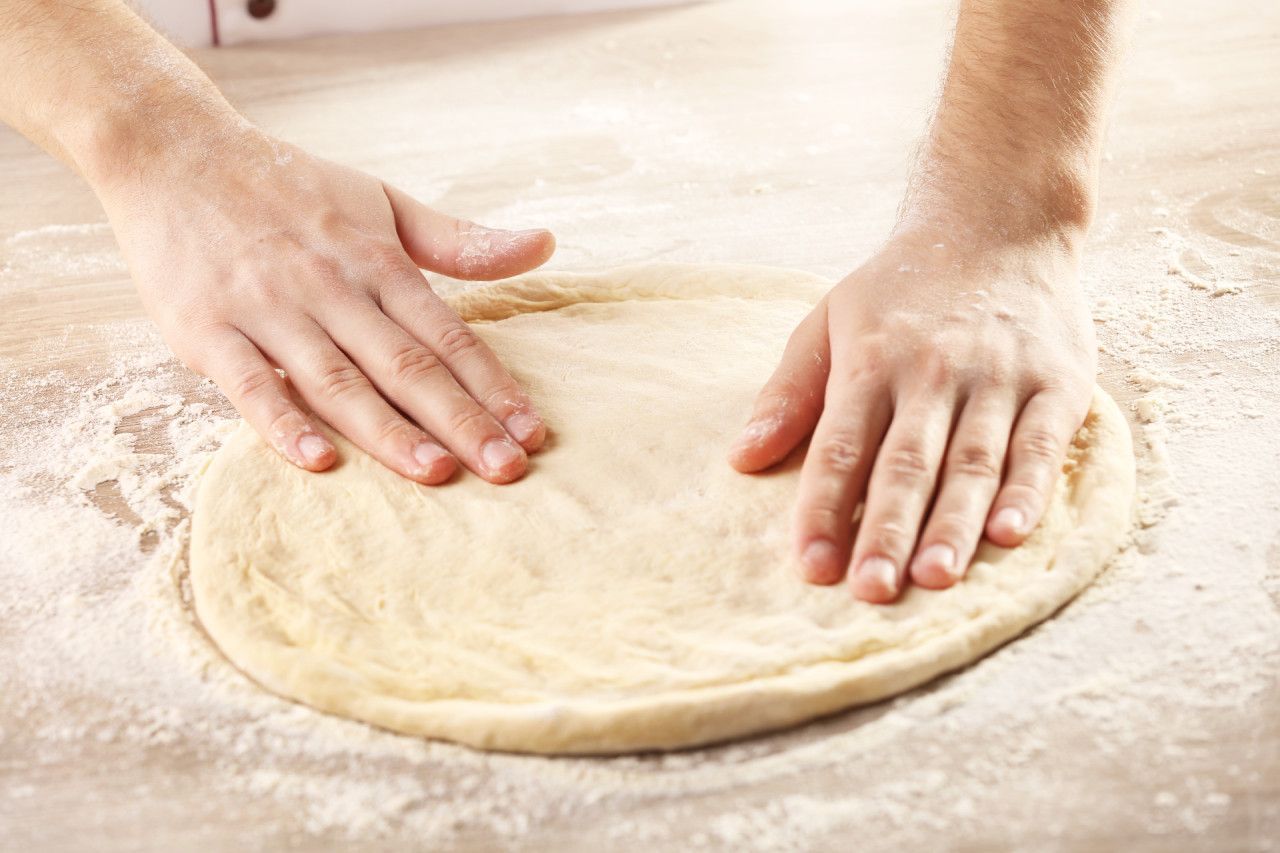 massa de pizza de longa fermentação sendo aberta à mão sobre mesa com farinha