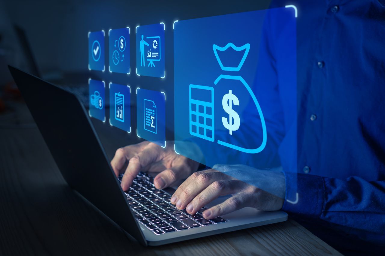 Uma pessoa está digitando em um laptop com uma sacola de dinheiro na tela.