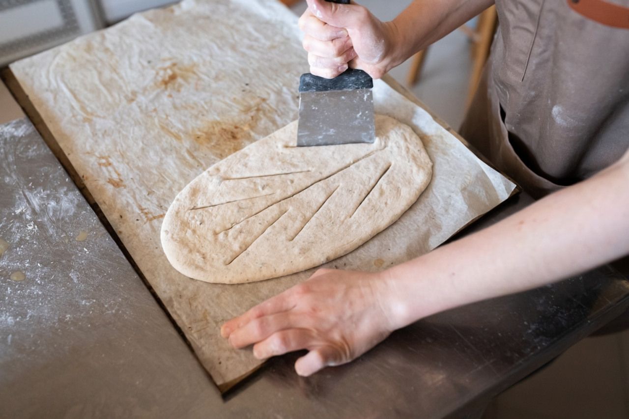 Uma pessoa está cortando um pedaço de massa com uma espátula.