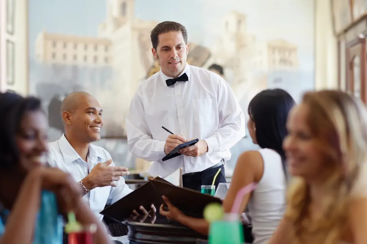 Um garçom está recebendo um pedido de um grupo de pessoas em um restaurante.